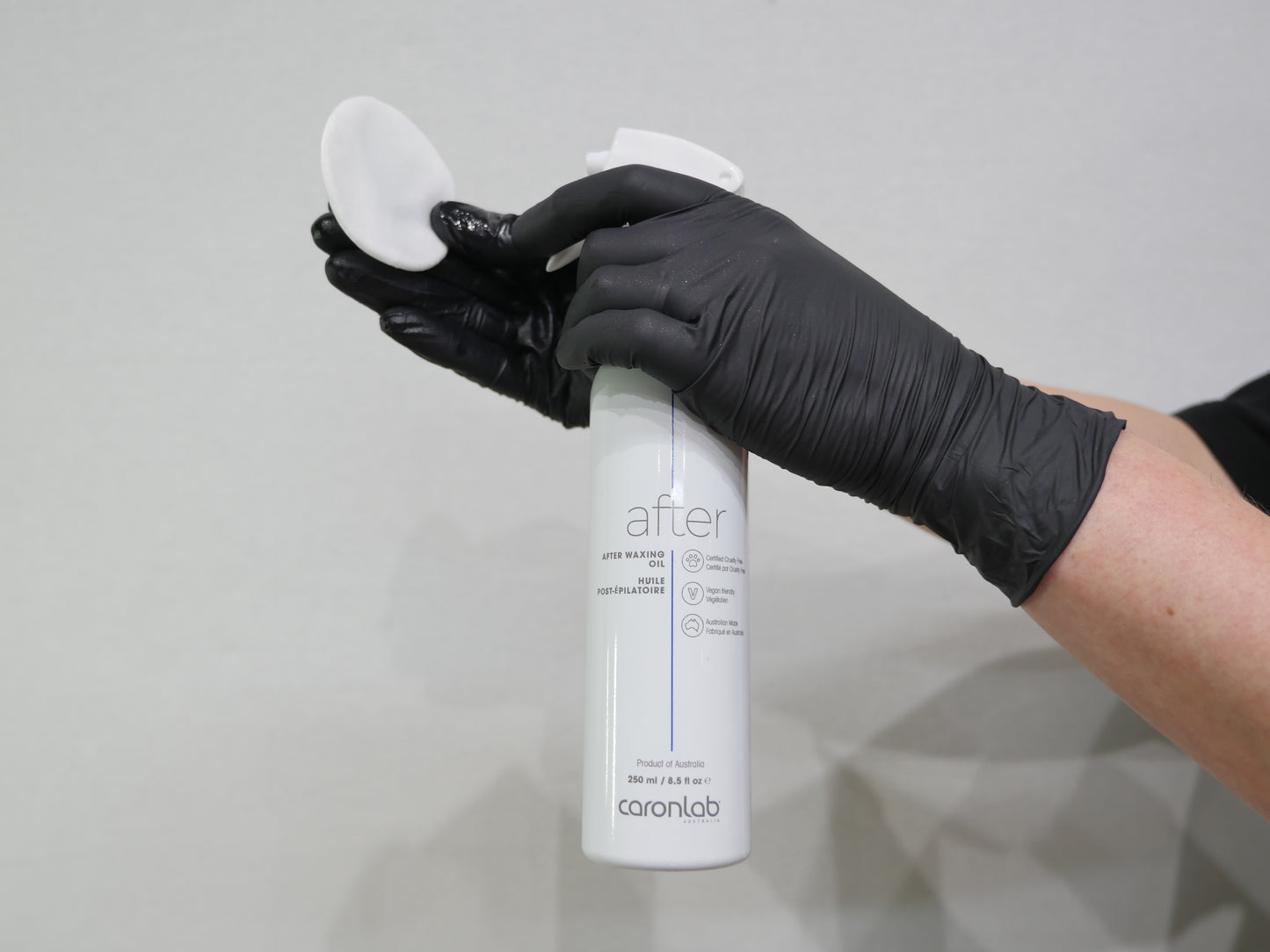 Person wearing black gloves holding a caronlab after waxing oil spray bottle against a gray background