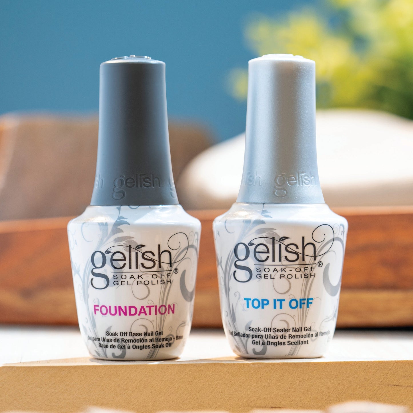 Two bottles of Gelish nail polish, 'Foundation' and 'Top It Off', on a wooden surface with a blurred background.