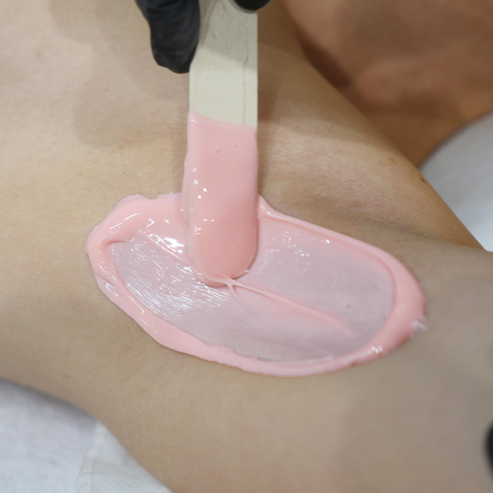 Caronlab Deluxe Strawberry Creme Hard Wax being applied during a professional waxing treatment on sensitive skin