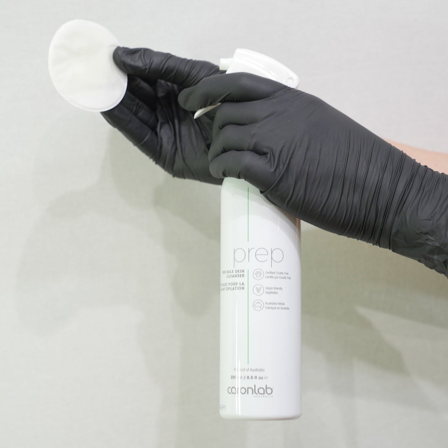 Person wearing a black glove holding a white spray bottle of caronlab prep - pre wax skin cleanser