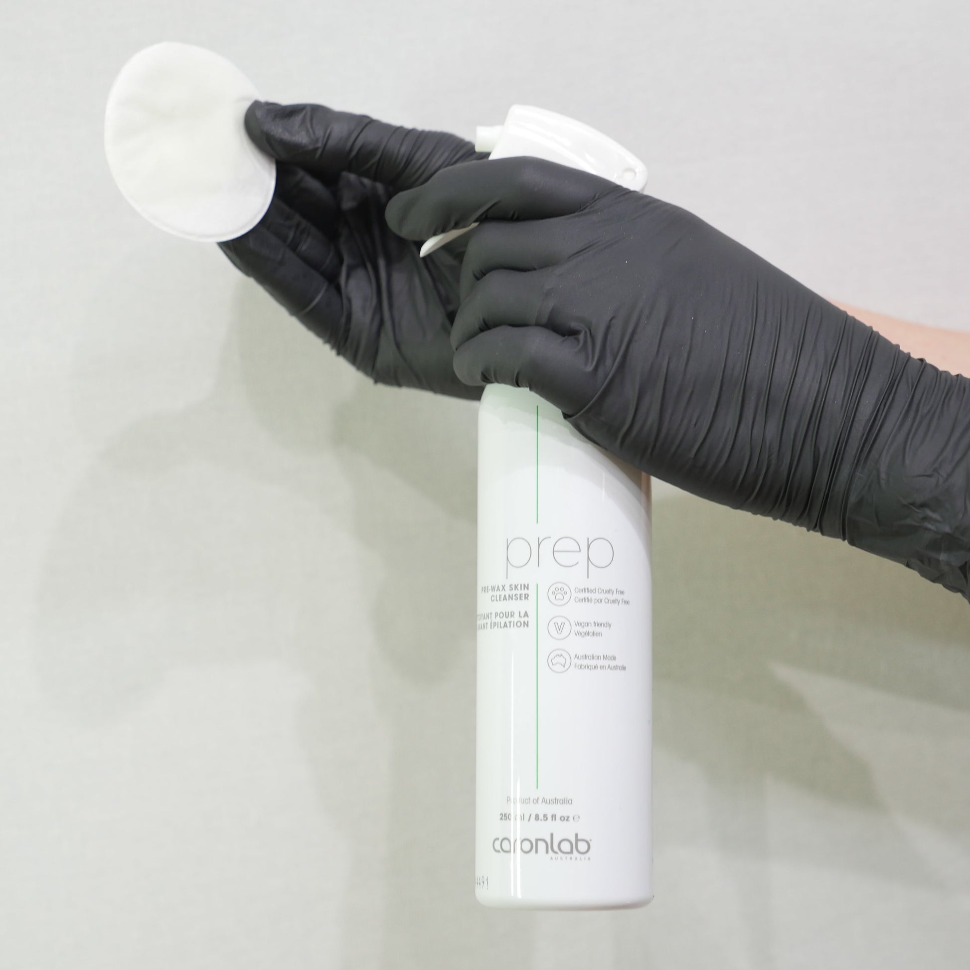 Person wearing a black glove holding a white spray bottle of caronlab prep - pre wax skin cleanser