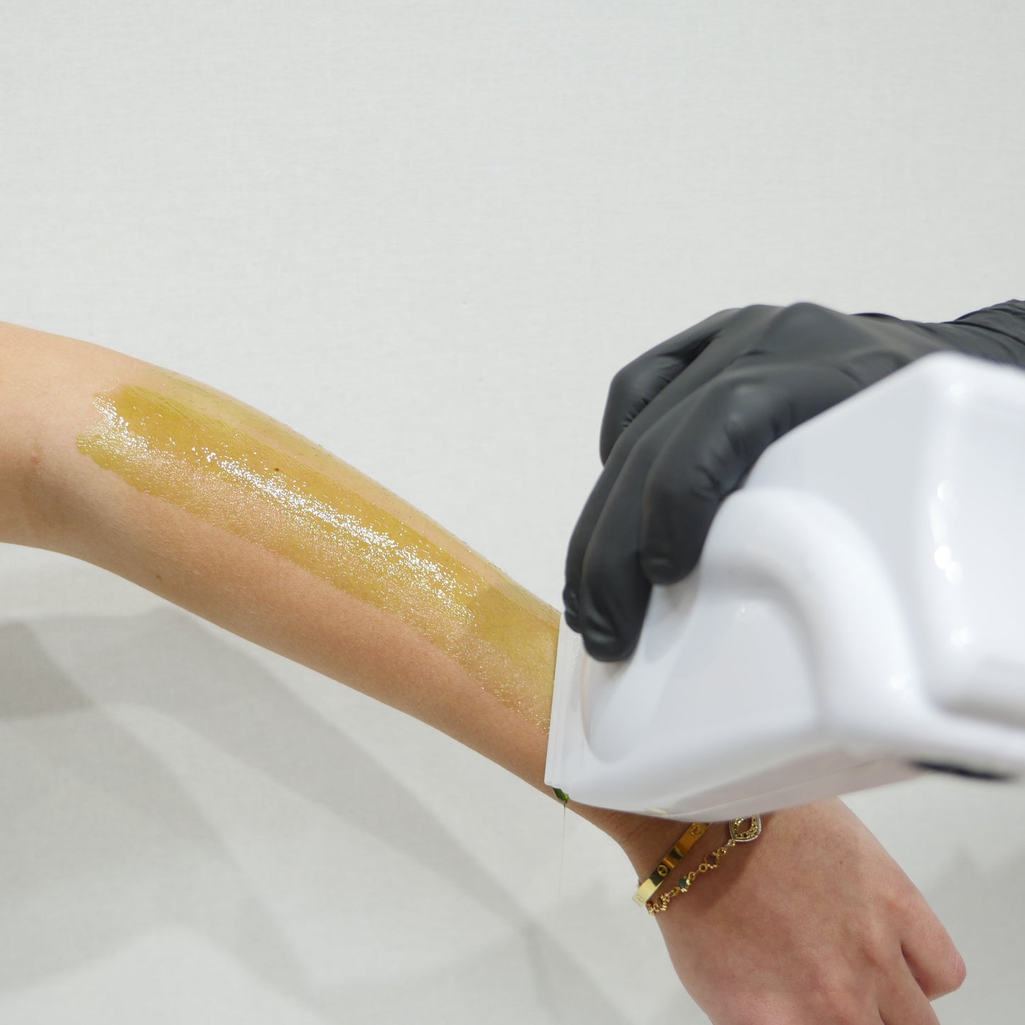 A close-up of a person's forearm with a strip of caronlab smooth & remove cartridge wax being applied via a cartridge wax heater.