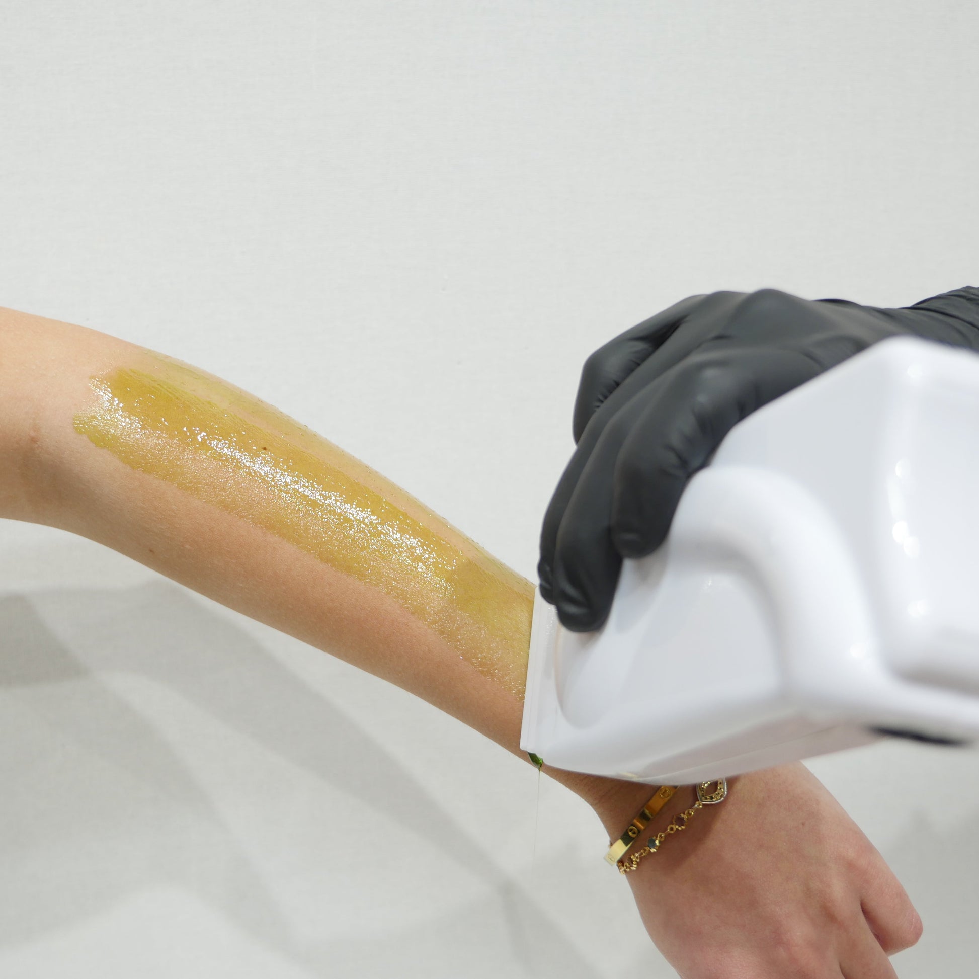 A close-up of a person's forearm with a strip of caronlab smooth & remove cartridge wax being applied via a cartridge wax heater.