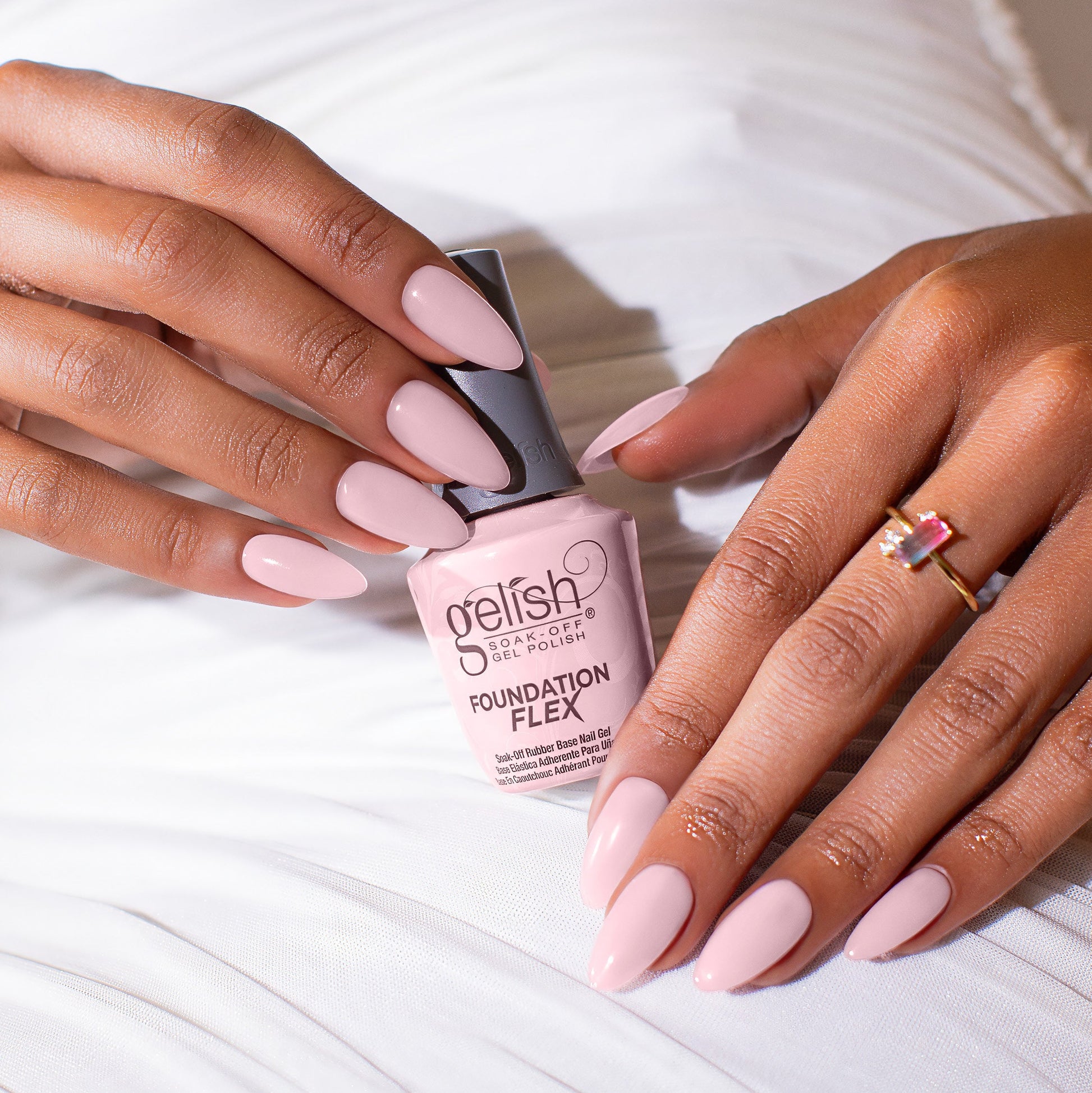 Person holding a bottle of Gelish foundation flex light pink with product on nails.
