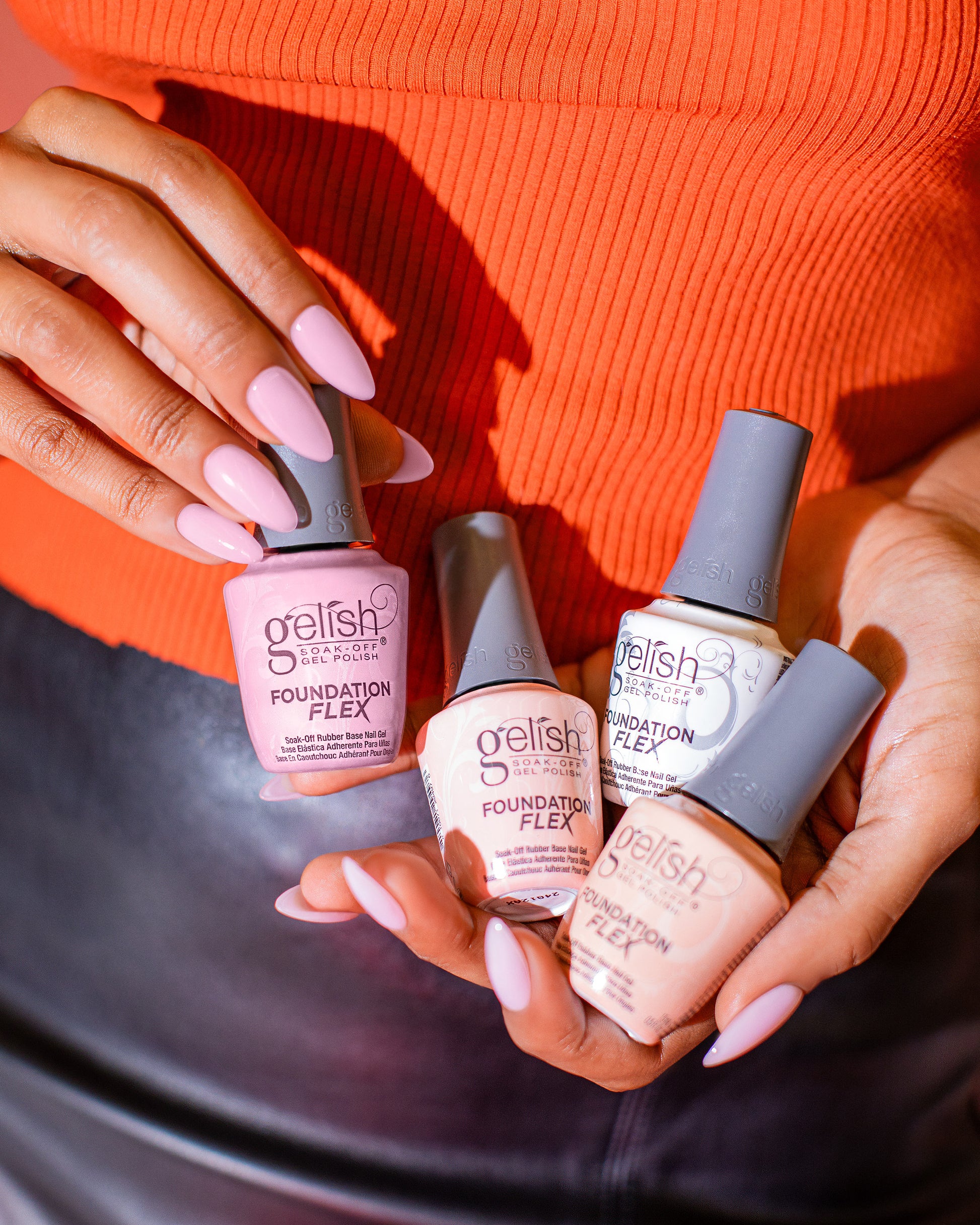 Gelish Foundation Flex rubber base coat colours held by a person with pink nails against an orange background