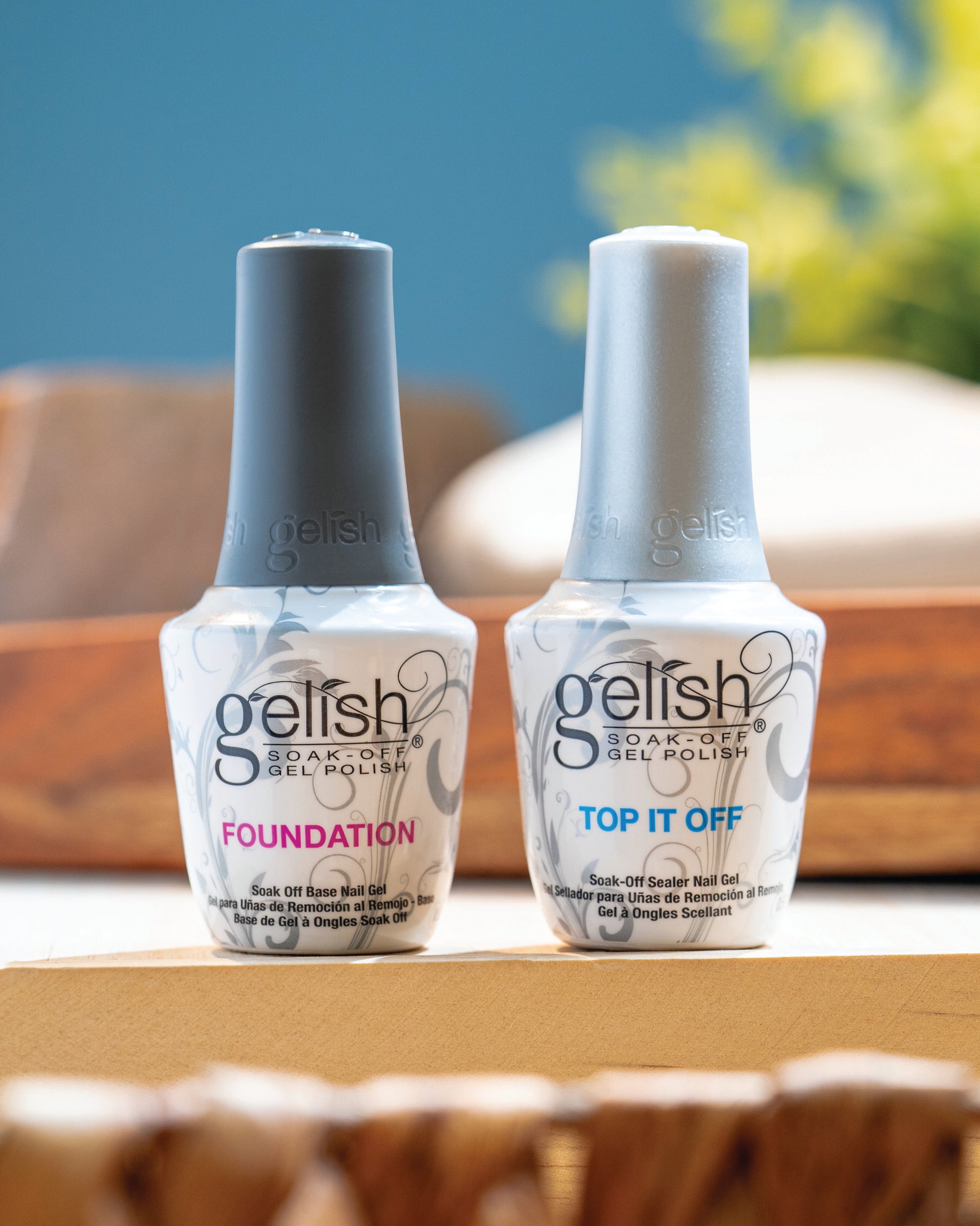 Two bottles of Gelish nail polish, 'Foundation' and 'Top It Off', on a wooden surface with a blurred background.