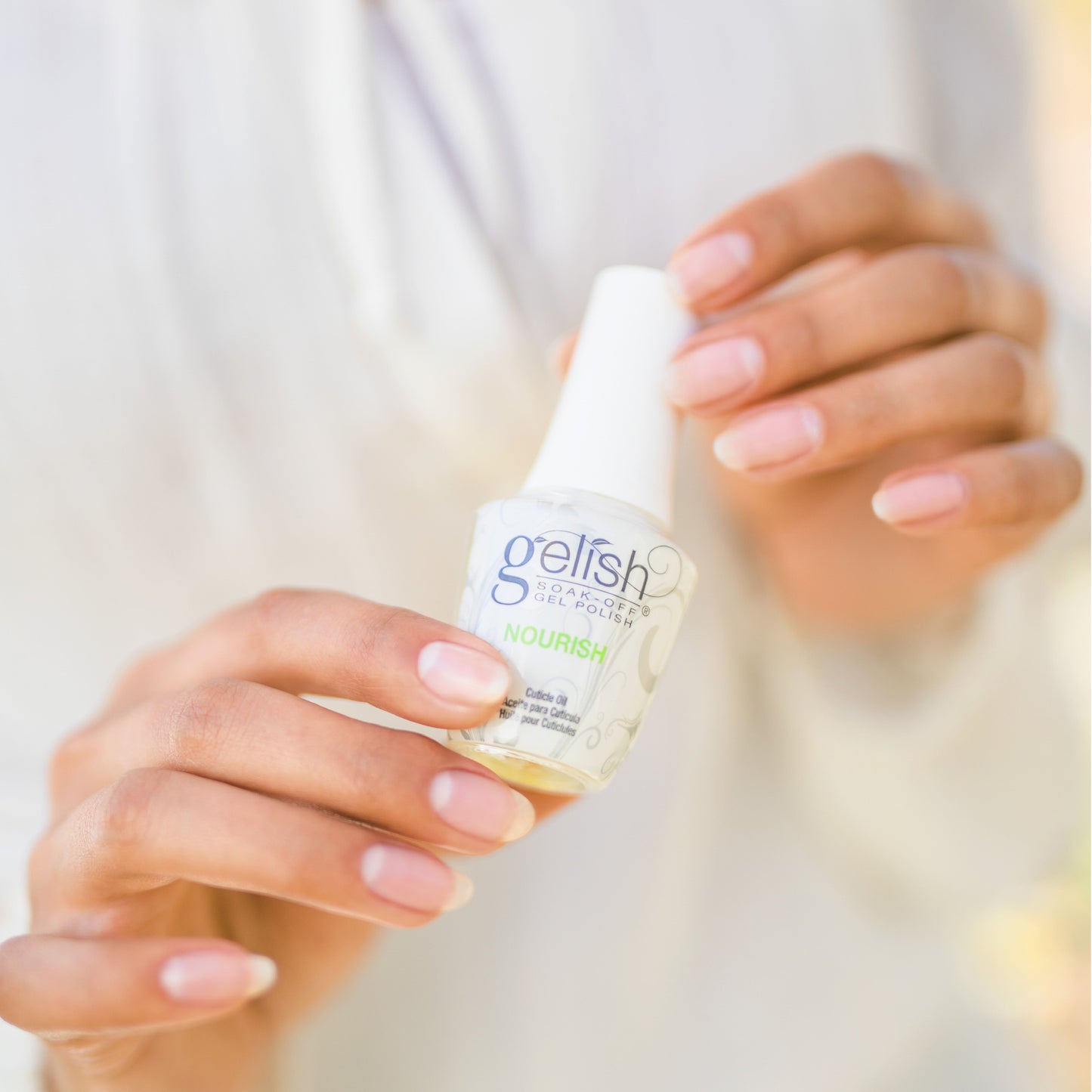 Hands holding Gelish Nourish Cuticle Oil to hydrate and condition cuticles as part of a professional nail care routine.